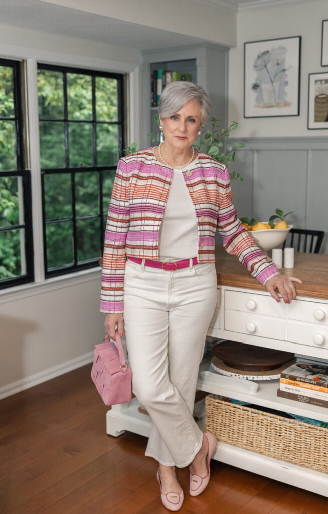 Woman over 50 wearing white tee under striped tweed jacket with white jeans and pink belt