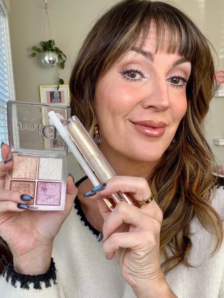 Woman holding Dior highlighter quad and Anastasia Beverly Hills shimmer lip gloss in Honey Diamond along with white eyeliner, showing finished Cloud Dancer inspired makeup look