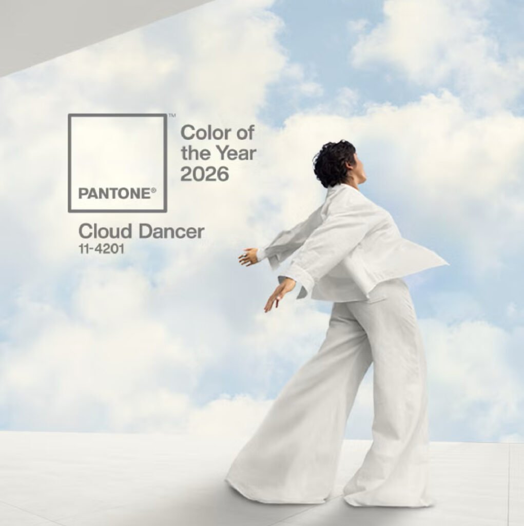 Pantone Color of the Year 2026 announcement graphic featuring Cloud Dancer 11-4201 with model in flowing white outfit against blue sky and clouds backdrop