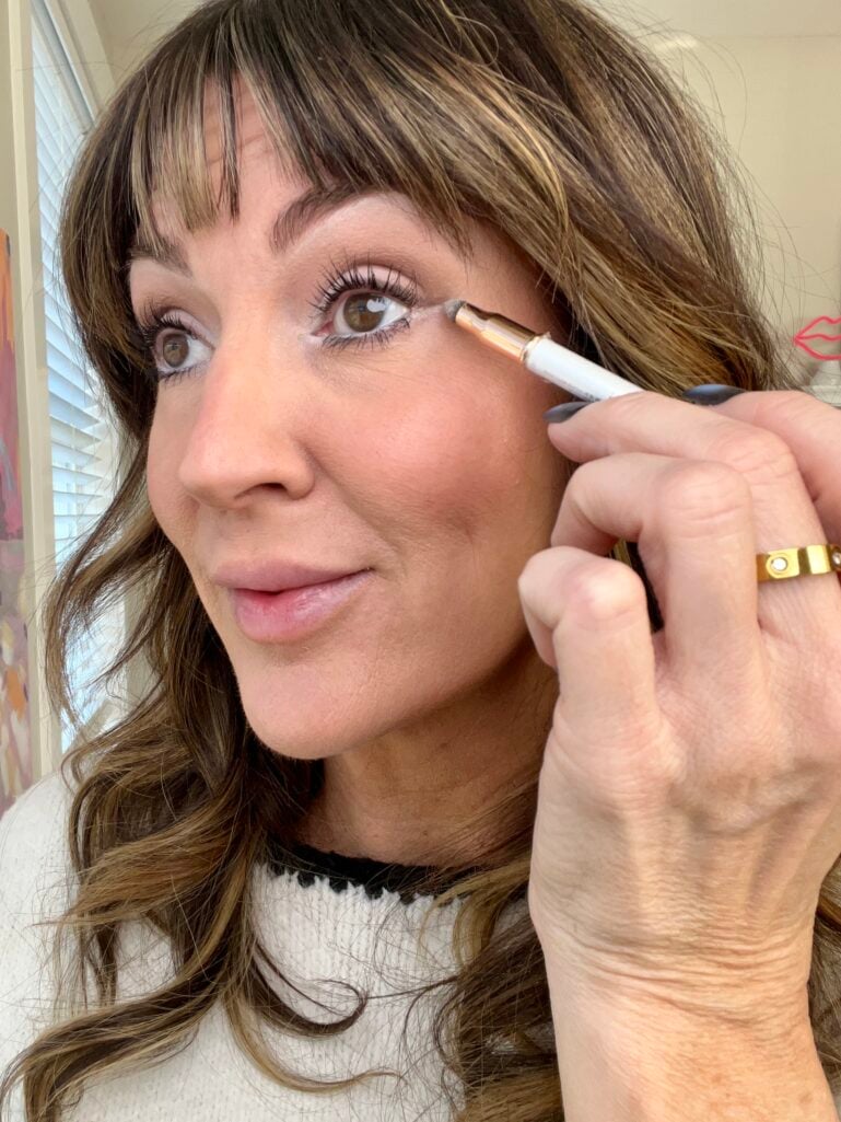 Woman applying white eyeliner to outer corner of eye between upper and lower lashes, showing Sophia Loren-inspired eye widening technique