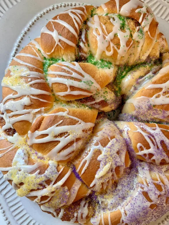 Overhead view of a frosted Mardi Gras King Cake decorated with purple, green, and gold sugars on a white platter