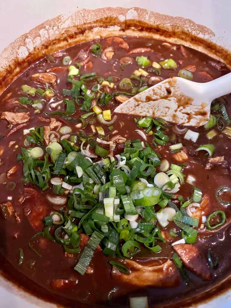 Adding sliced scallions to the finished gumbo in the Dutch oven