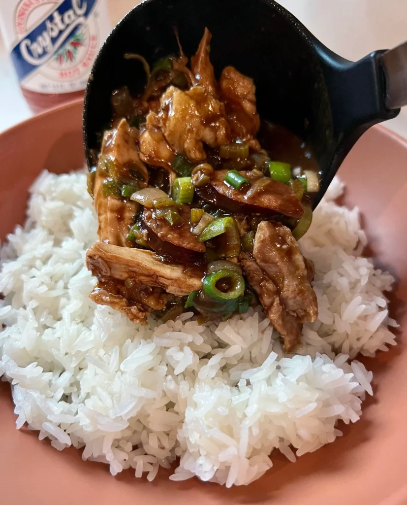 Ladling chicken and sausage gumbo over white rice in a terracotta bowl with Crystal hot sauce in the background