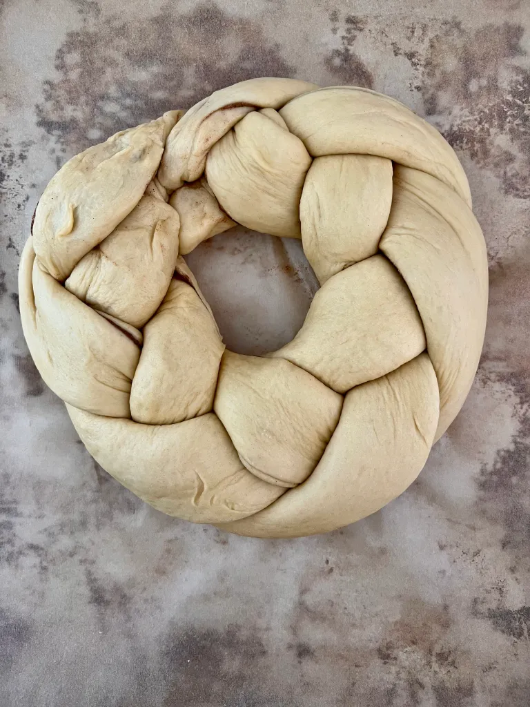 Braided King Cake dough shaped into an oval ring on a parchment-lined sheet pan before rising