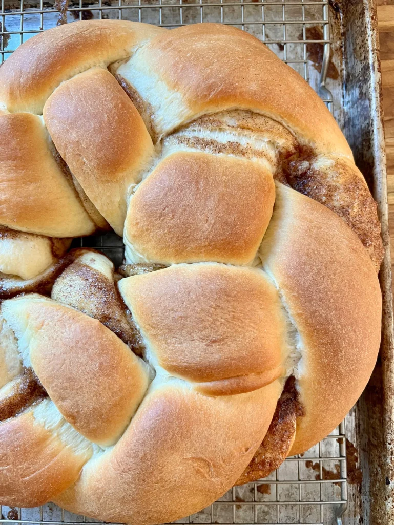 Golden baked King Cake cooling on a wire rack with cinnamon filling visible in the braid
