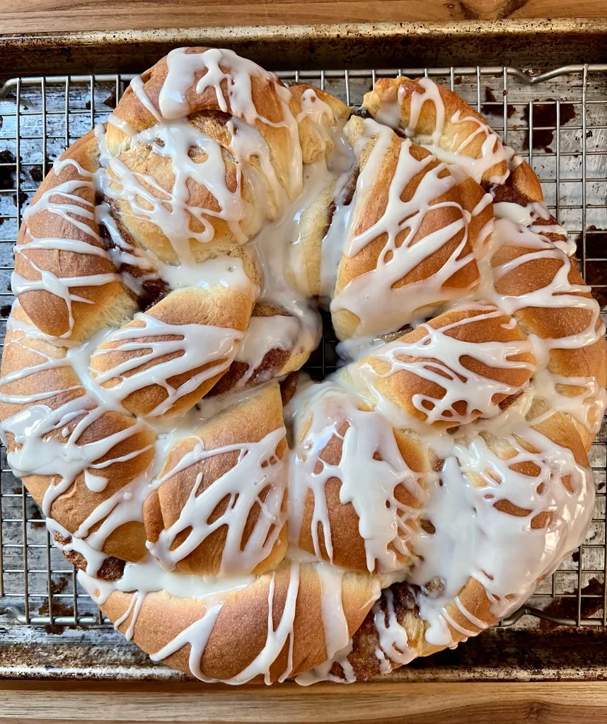 Baked King Cake drizzled with vanilla icing on a wire rack