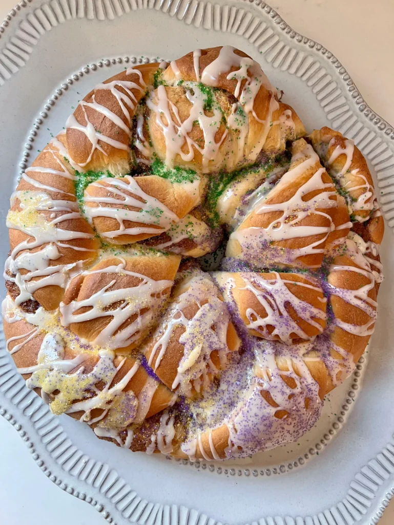 Finished King Cake on a white platter decorated with purple, green, and gold sugars over the icing