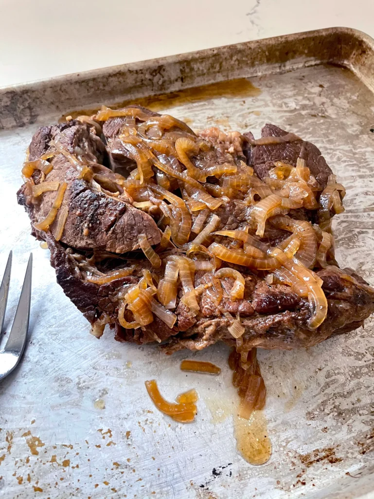Tender cooked chuck roast topped with caramelized onions on a sheet pan with a fork