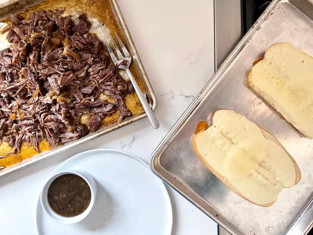 French Dip assembly station with shredded beef, provolone-covered hoagie rolls, and a ramekin of au jus