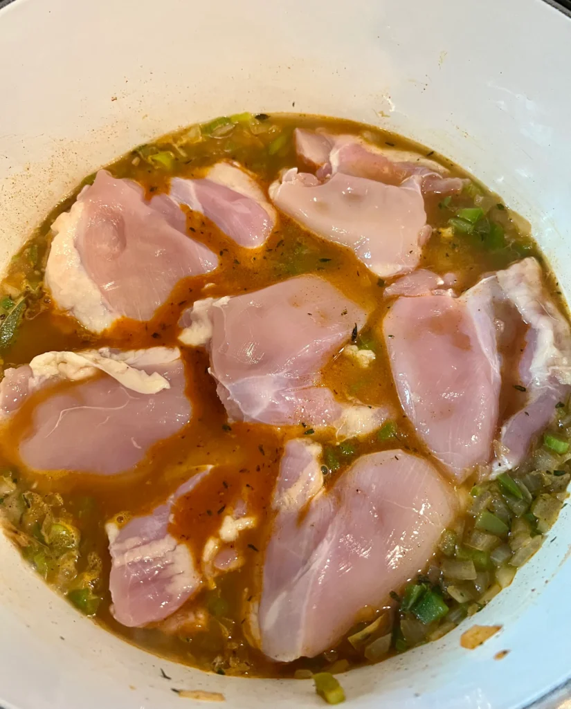 Chicken thighs nestled into the seasoned broth and vegetables in the Dutch oven