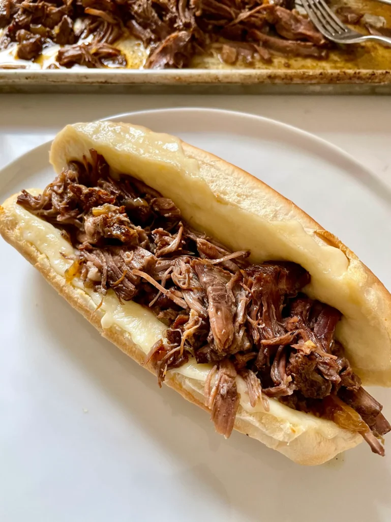 Open hoagie roll filled with shredded beef and melted provolone on a plate