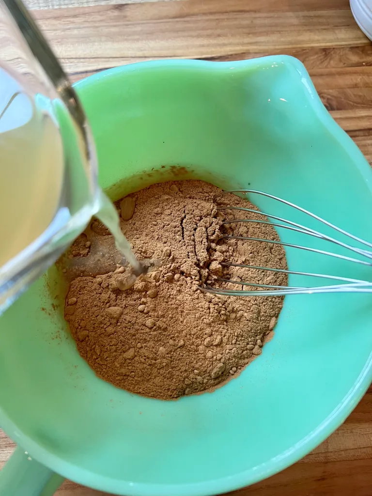 Whisking chicken broth into toasted flour in a jadeite mixing bowl to make the roux