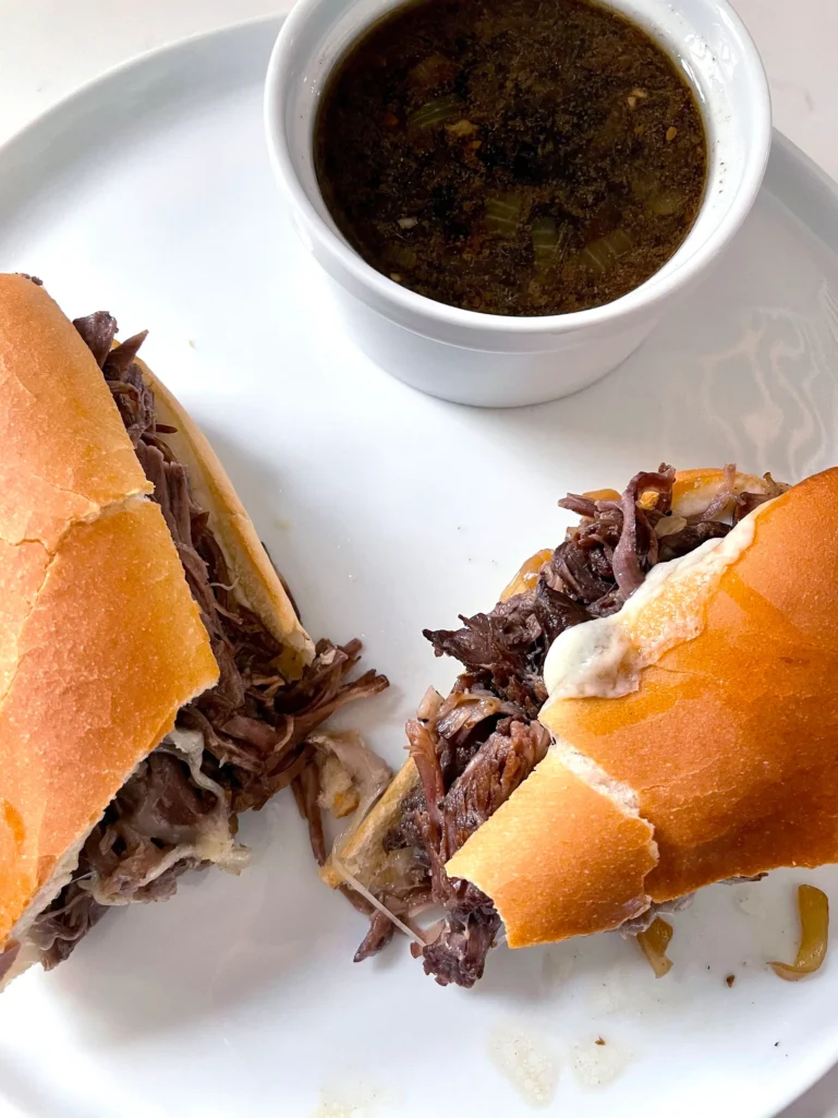 Overhead view of sliced French Dip sandwich with shredded beef and melted provolone, served with au jus