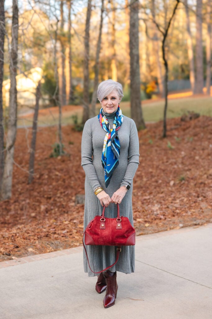 Beth in a gray ribbed sweater dress with a colorful silk scarf, burgundy boots, and a red suede handbag — adding pops of red through accessories