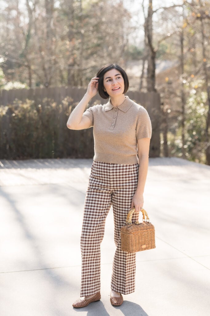 Kelly in a camel cashmere polo sweater with brown and white gingham pants, woven flats, and a wicker bamboo-handle bag — a warm-toned take on spring gingham for petites