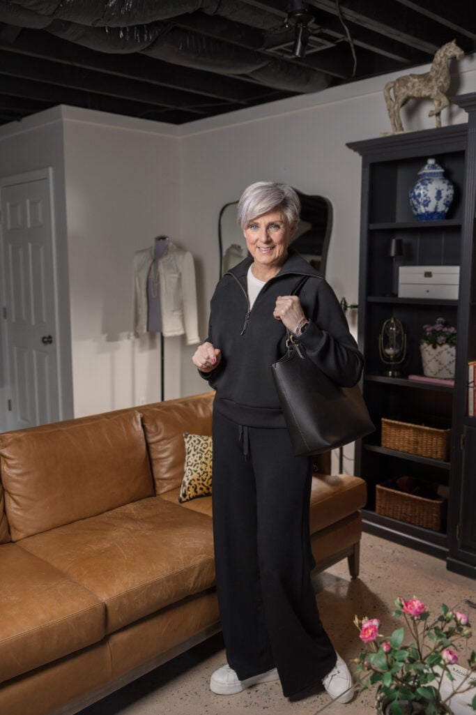 Beth Djalali wearing a black Spanx AirEssentials half-zip hoodie and wide-leg pants with white sneakers and a black leather tote — modern grandmother style that's comfortable and polished.