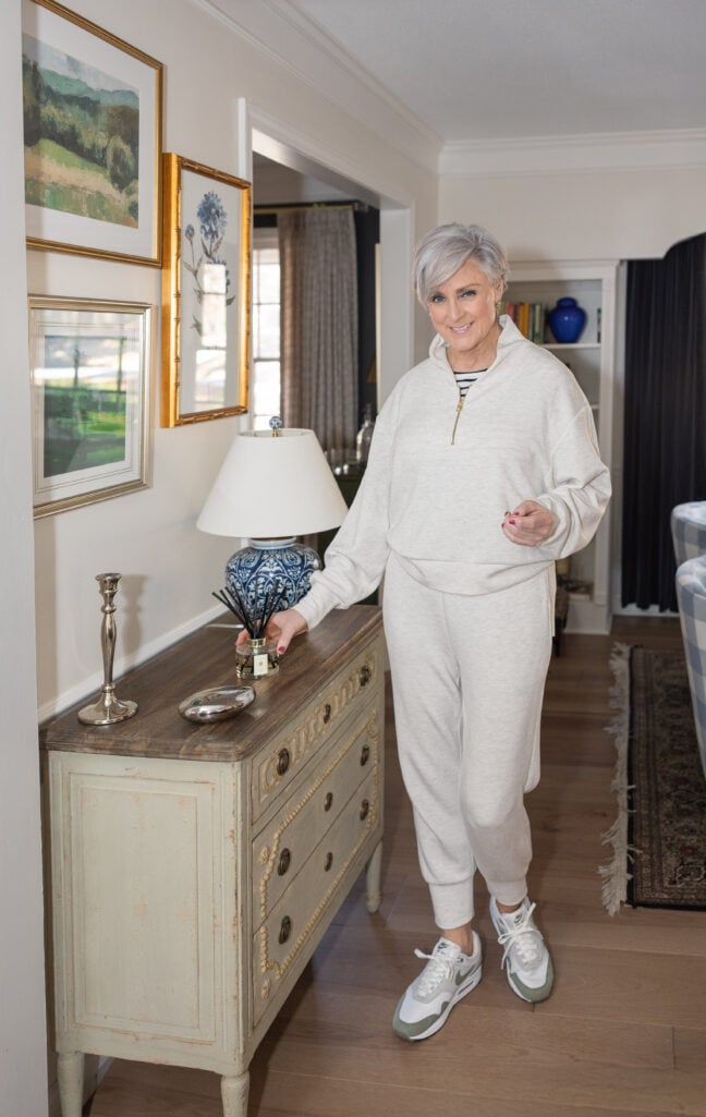 Beth Djalali wearing a cream Spanx Air Essentials half-zip pullover with matching joggers and Nike Air Max sneakers, standing in her home — elevated athleisure for stylish grandmothers over 60.