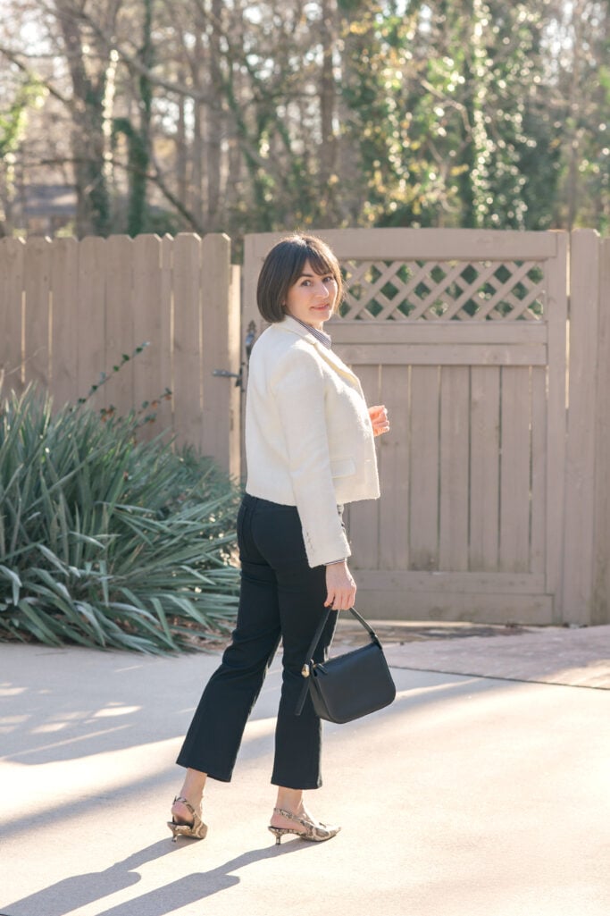 Back view of Kelly walking in ivory bouclé blazer, black Spanx petite kick flare jeans, and snake-embossed leather slingback heels — showing how kick flare jeans create a balanced petite silhouette
