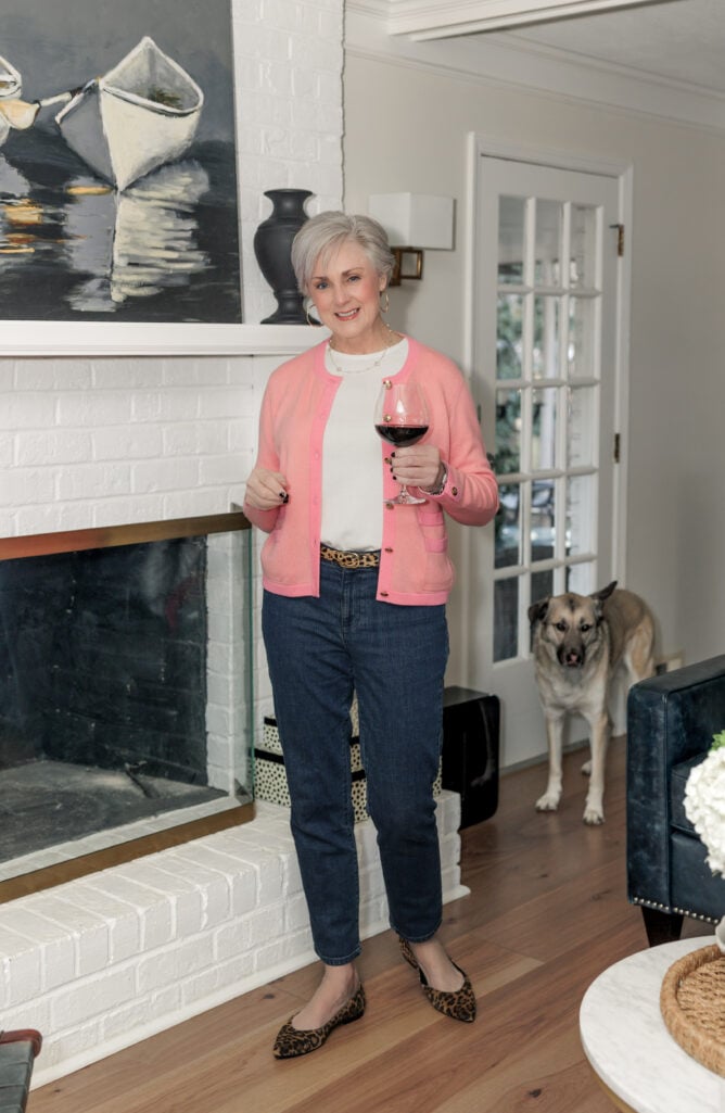 Casual chic outfit for women over 50 featuring pink cardigan, white tee, dark jeans, and leopard flats