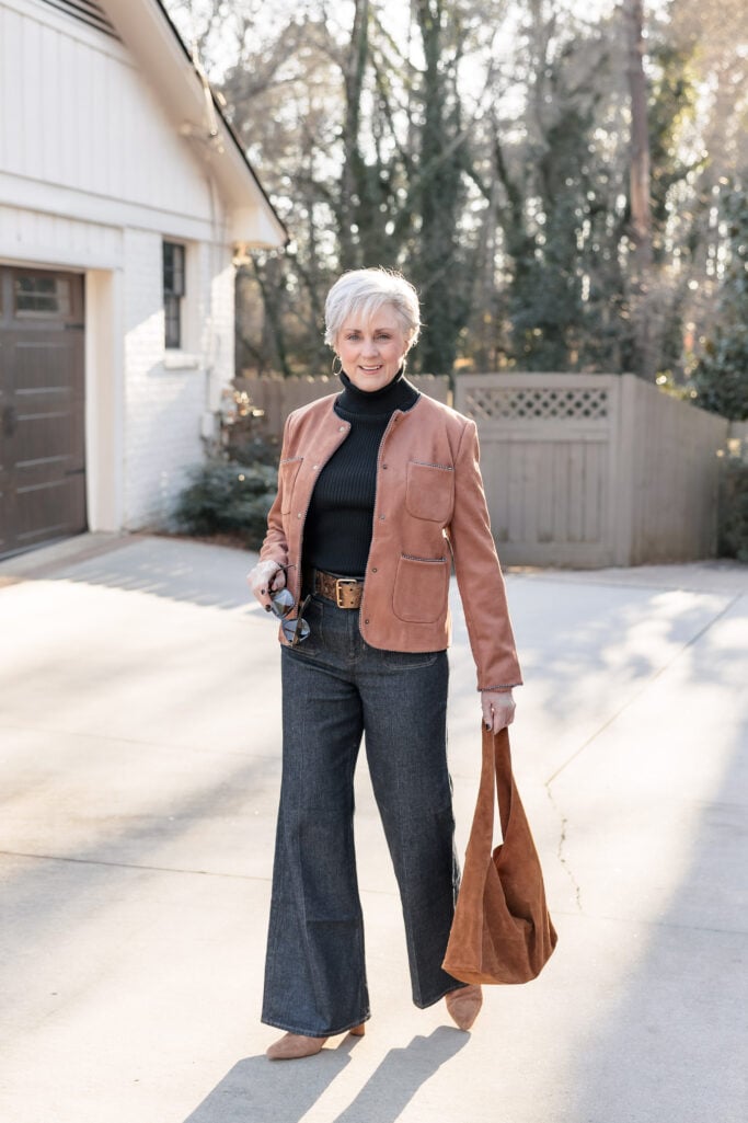 Woman over 50 wearing cognac leather jacket with black turtleneck and wide-leg jeans for casual chic style