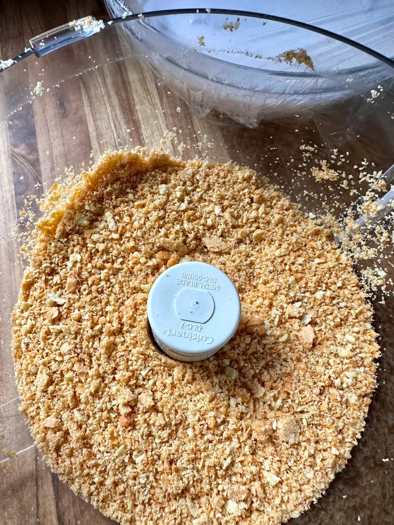 Crushed Cheez-It cracker breading in a food processor bowl pulsed to a coarse sandy texture