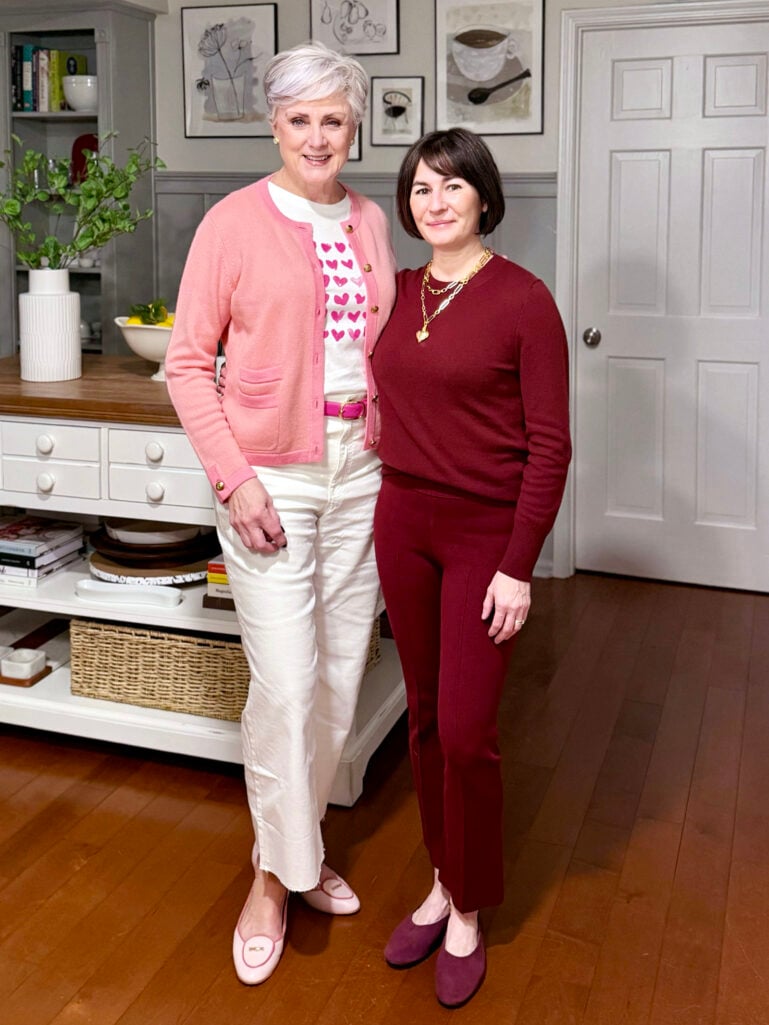 Full-length view of Beth and Kelly standing side by side in front of the kitchen island, Beth in pink and white and Kelly in head-to-toe burgundy with plum ballet flats