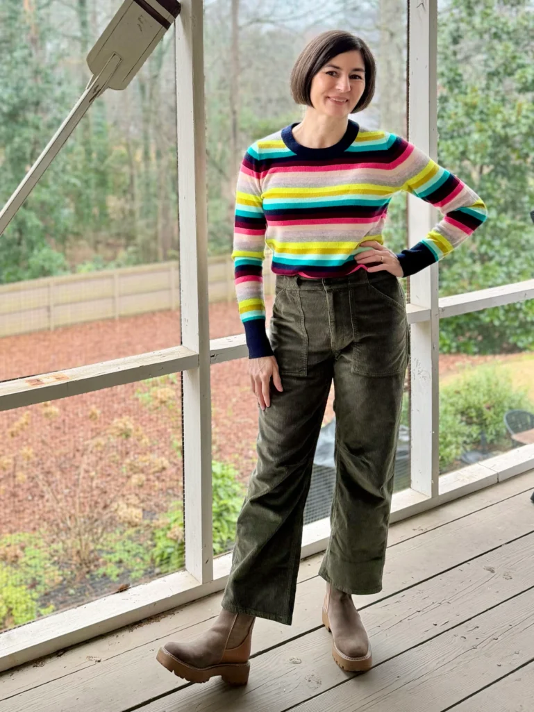 Woman styling a bold multicolor rainbow horizontal striped sweater with olive green corduroy wide-leg utility pants and taupe chunky Chelsea boots, demonstrating how to wear colorful stripes over 50.