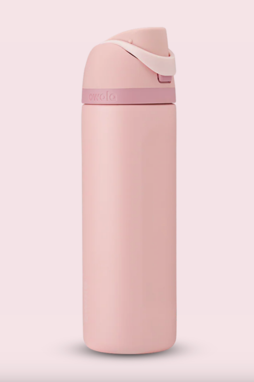 Blush pink Owala insulated stainless steel water bottle with a flip-top lid and built-in carry loop, shown against a soft pink background.