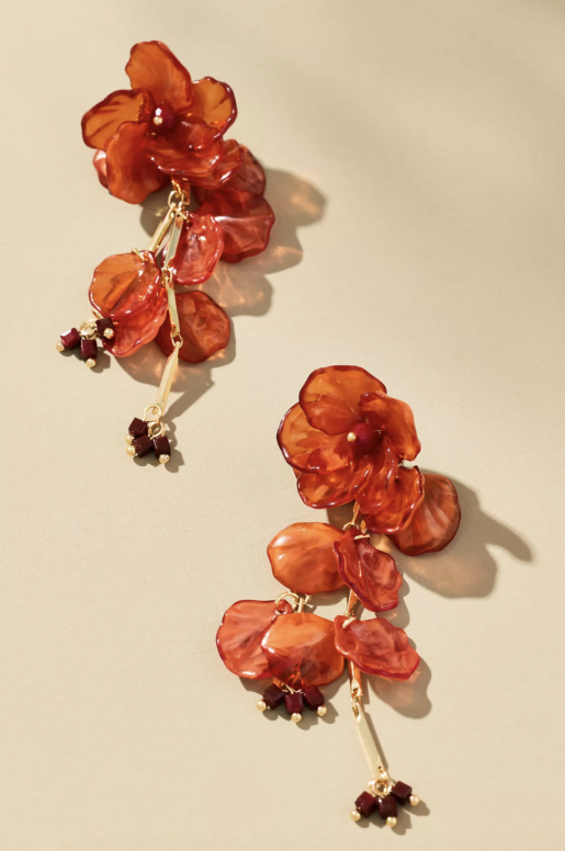 Vibrant orange floral drop earrings featuring layered translucent petals with gold-tone centers and dangling bead accents. Long statement earrings with a sculptural, botanical-inspired design.
