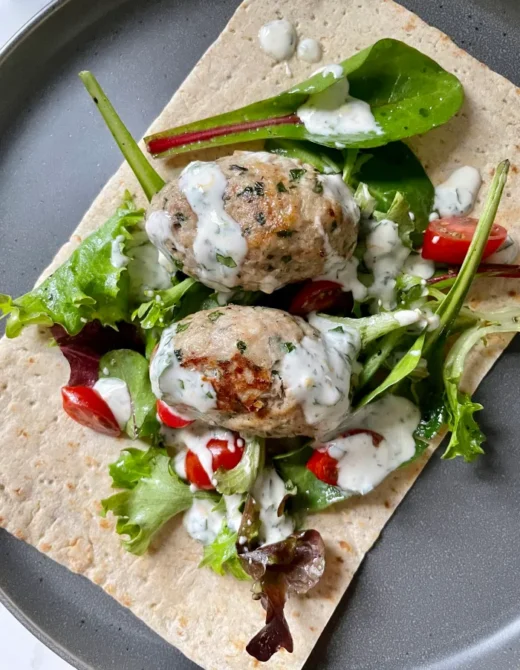 Overhead view of chicken kofta wrap with mixed greens, grape tomatoes, and yogurt sauce on lavash flatbread on a gray plate