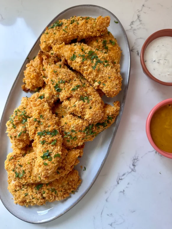 Baked Cheez-It chicken tenders on an oval platter garnished with parsley, served with ranch and honey mustard dipping sauces