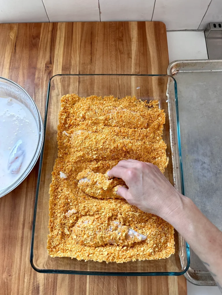 Breading station with hand dredging buttermilk-coated chicken tenders in crushed Cheez-It breading