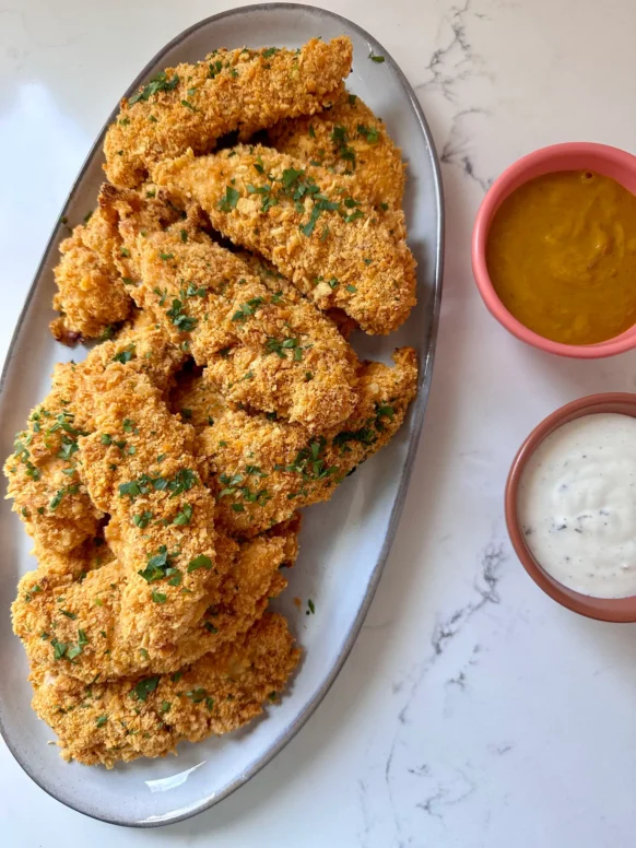 Baked Cheez-It chicken tenders on an oval platter garnished with parsley, served with ranch and honey mustard dipping sauces