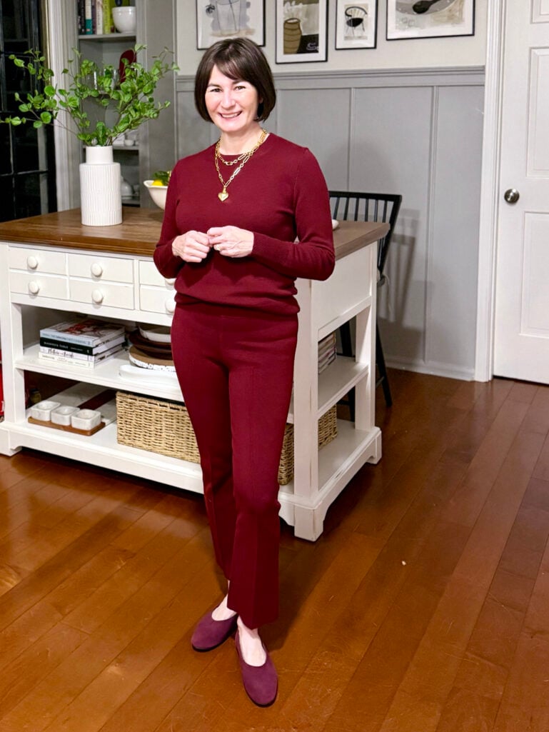 Full-length view of Kelly in her monochromatic burgundy outfit with plum ballet flats, standing in front of the kitchen island with her hands together