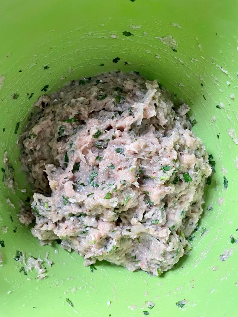 Chicken kofta mixture fully combined with herbs and spices in a green mixing bowl