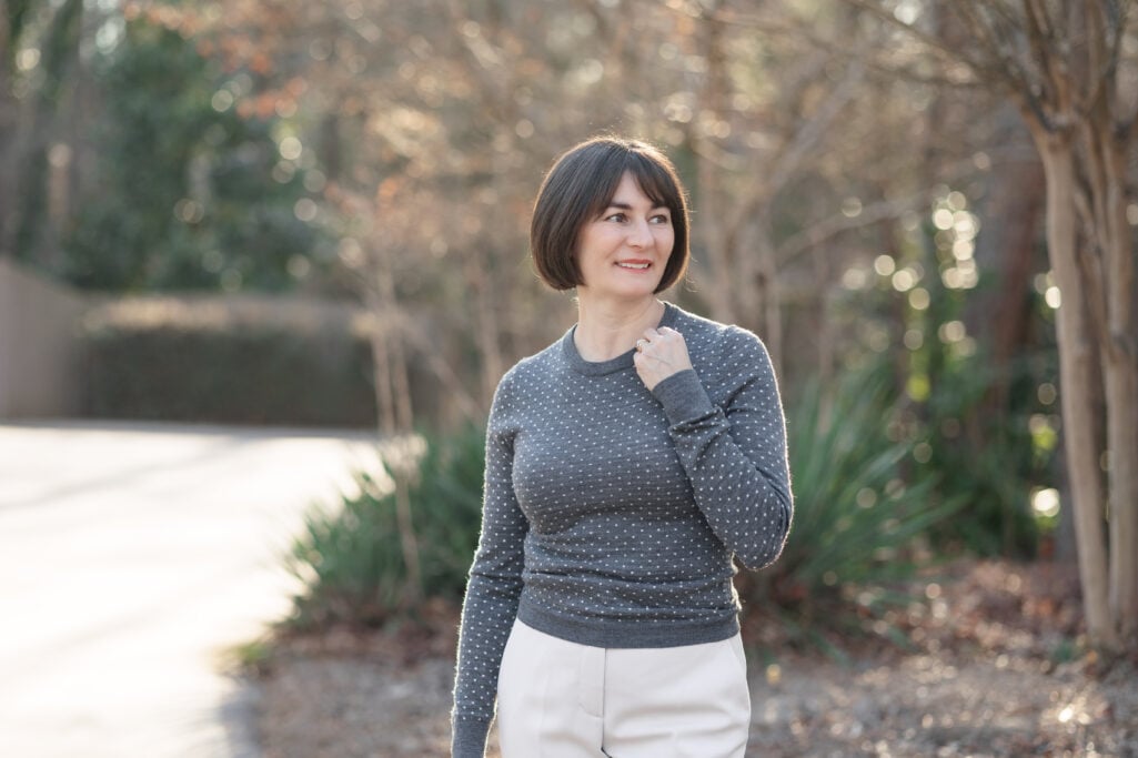 Landscape close-up of Kelly in charcoal polka dot fitted crewneck sweater with cream pants — showing small-scale dot print and fitted silhouette ideal for petite frames