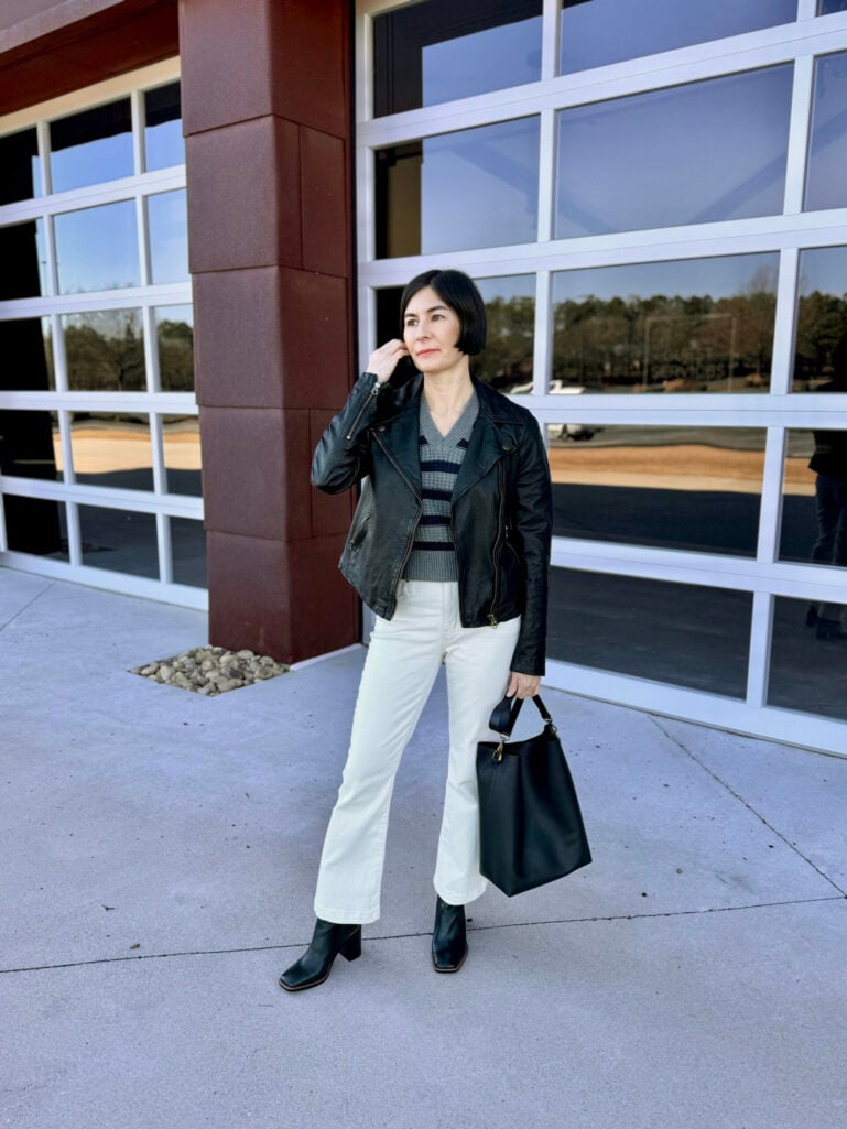 Kelly styling a black leather moto jacket over a striped sweater with white flare pants and black boots