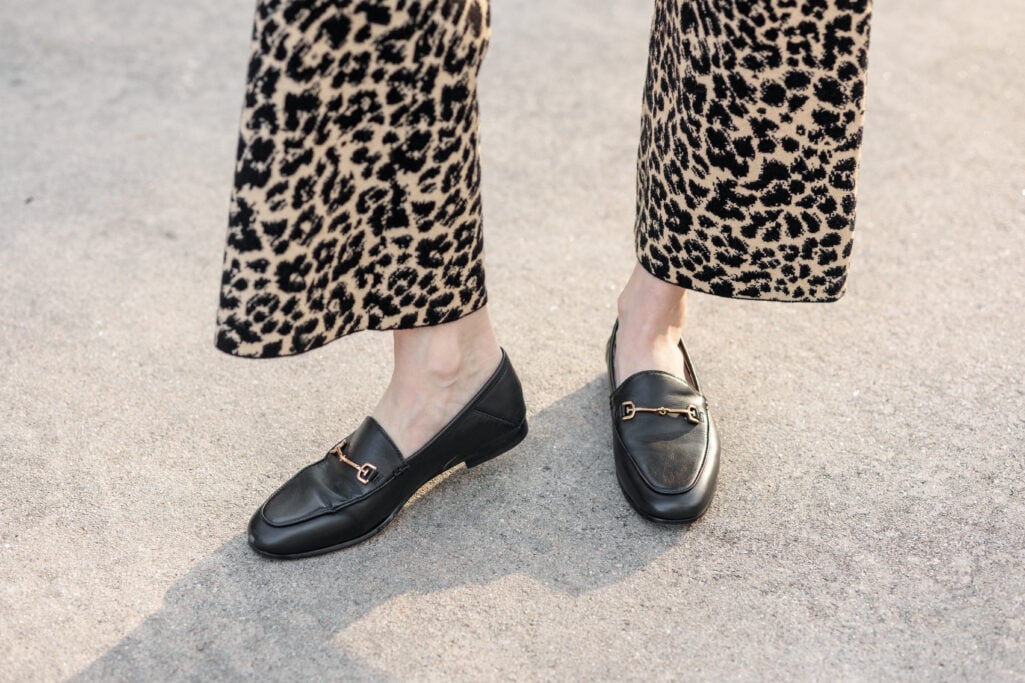 Close-up of black leather loafers with gold horsebit hardware worn with leopard print midi skirt