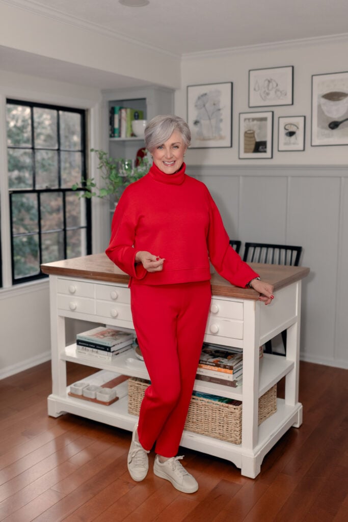 Beth in a red turtleneck and matching red joggers with white sneakers, leaning against a kitchen island — monochromatic red outfit for women over 50