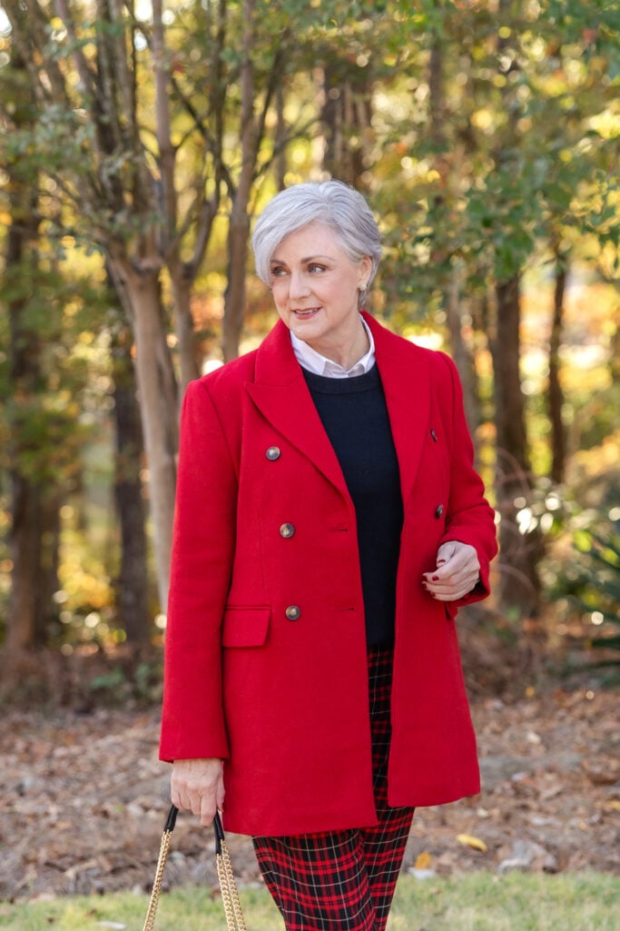 Beth in a red double-breasted pea coat layered over a navy sweater, white button-down, and red plaid pants outdoors — red coat styled with plaid pants