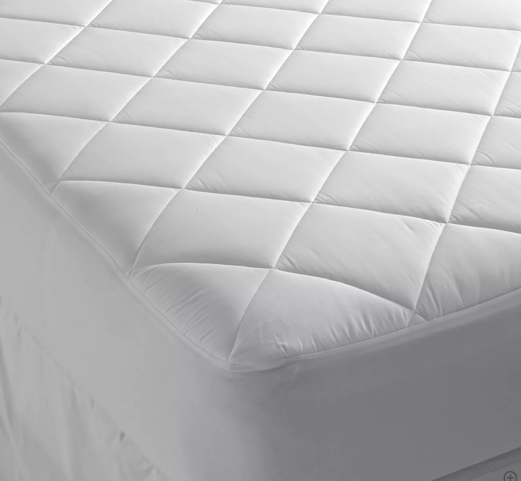 White quilted mattress pad with stitched square pattern, fitted smoothly over a mattress corner to show thickness and padded texture.