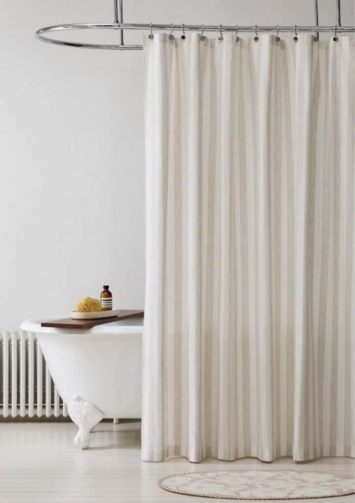 West Elm cotton-linen blend shower curtain in neutral cream with subtle vertical stripe texture, hung from chrome curtain rod for an airy modern bathroom look.
