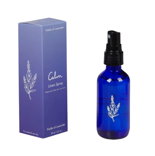 Lavender linen spray in a cobalt blue glass bottle with black spray top, shown beside a purple box labeled “Calm Linen Spray – Fields of Lavender.”