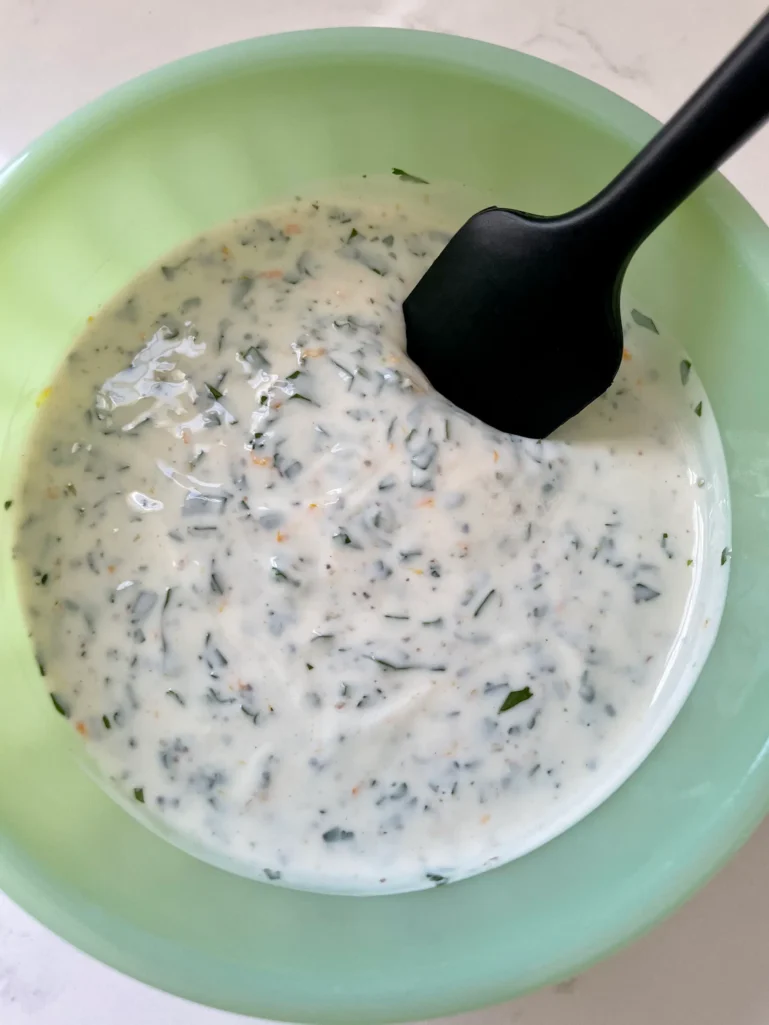 Finished yogurt sauce with herbs and orange zest stirred together in a green bowl with a black spatula