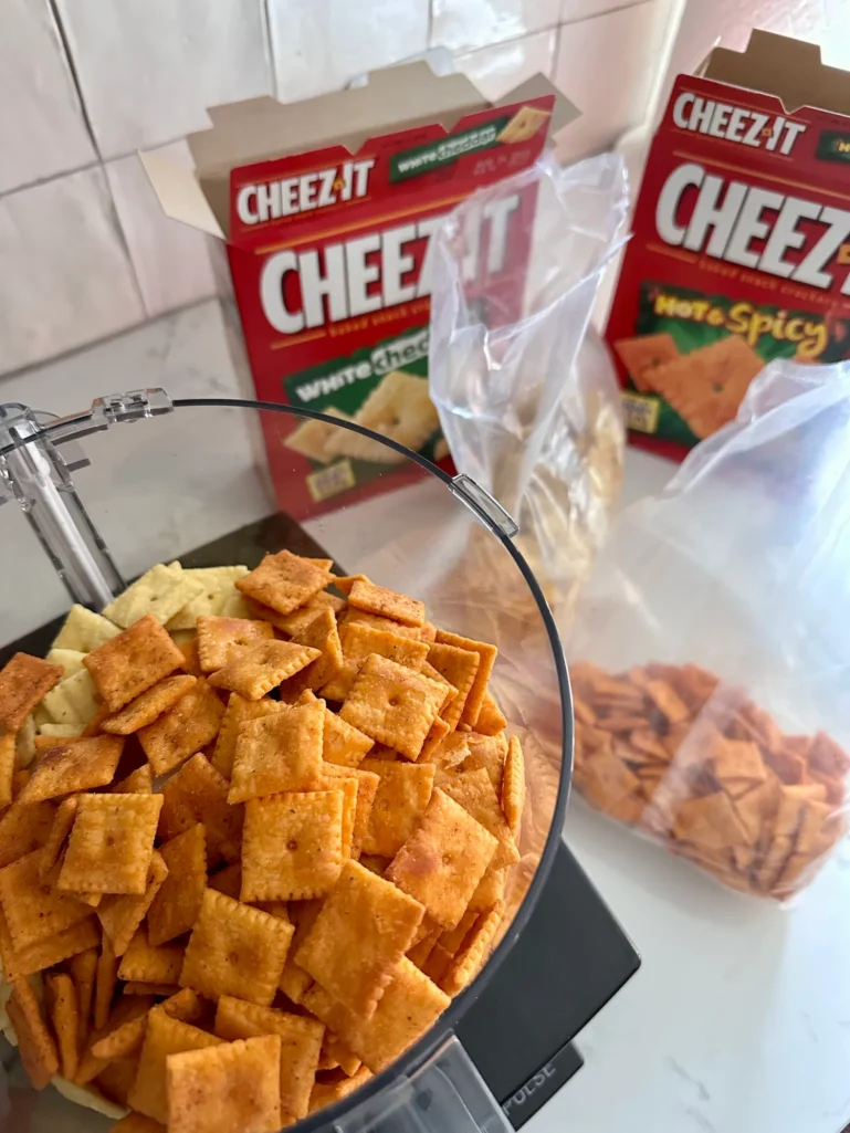 Food processor bowl filled with Hot & Spicy and White Cheddar Cheez-It crackers with boxes in the background