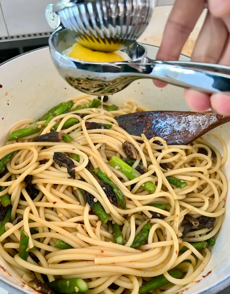 Squeezing fresh lemon juice through a citrus press over the pot of bucatini tossed with asparagus, morels, and crushed red pepper