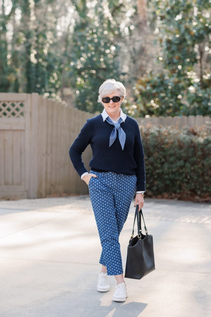 Navy sweater layered over a white collared shirt with a scarf, patterned pants, and white sneakers.