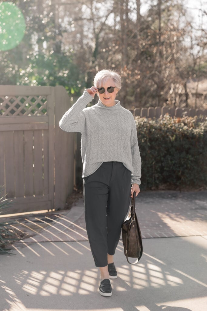 Classic style over 50 outfit with a gray cable knit sweater, charcoal tailored pants, and black loafers.