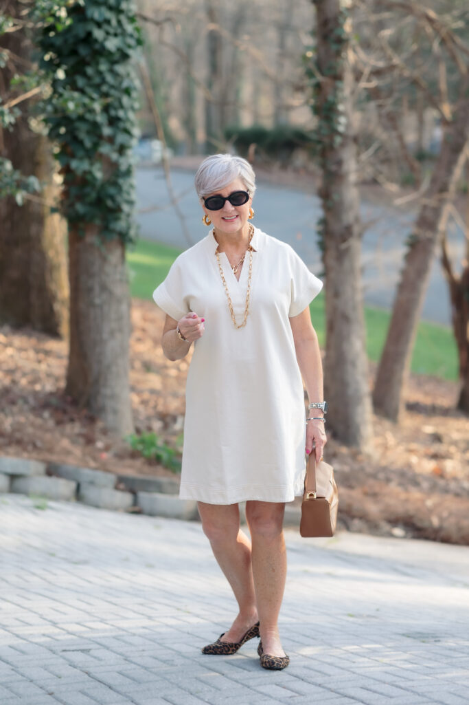 Woman over 50 wearing ivory polo shift dress with leopard kitten heel slingbacks and tan structured bag — spring dress outfit idea