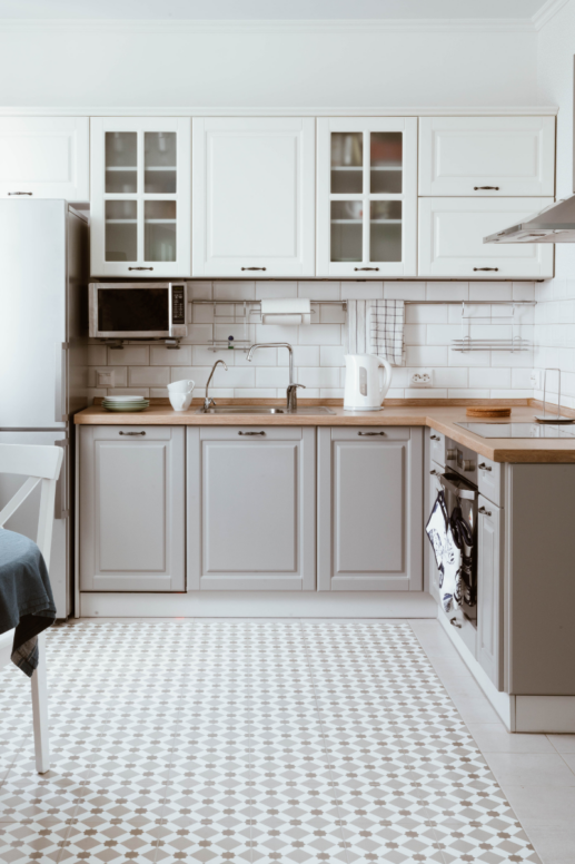 Bright white kitchen with shaker cabinets, wood countertops, subway tile backsplash, and patterned tile flooring, styled as a clean and organized cooking space.